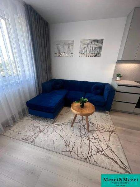 Wohnzimmer mit blauem Sofa, Tisch, Vorhängen und Holzboden.