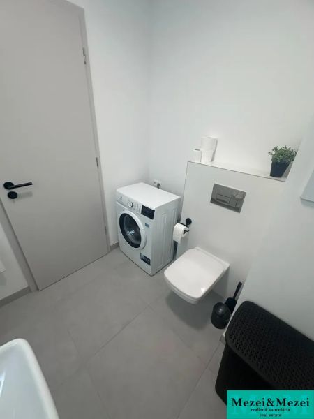 Badezimmer mit Waschmaschine, Toilette und beigefarbenen Fliesen in einer 2-Zimmer-Wohnung.
