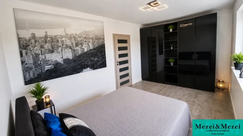 Schlafzimmer mit schwarzem Kleiderschrank, großem Foto und Zimmerpflanzen.