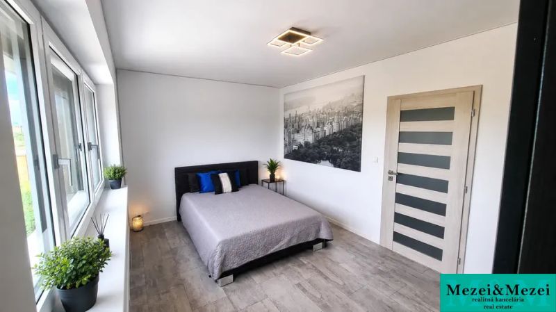 Schlafzimmer in einem Einfamilienhaus mit großem Fenster, Bett und Boden mit Holzdekor.
