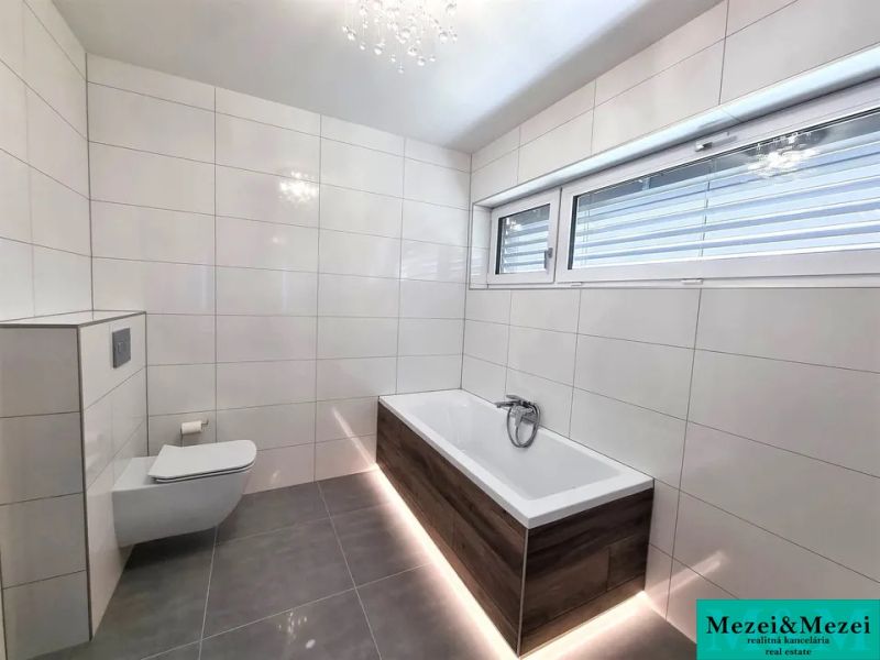 Badezimmer in einem Einfamilienhaus mit einer Badewanne in Holzoptik und einem großen Fenster.