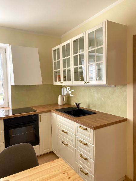 Küche in einer 3-Zimmer-Wohnung mit weißen Schränken und einem Boden in Holzoptik.