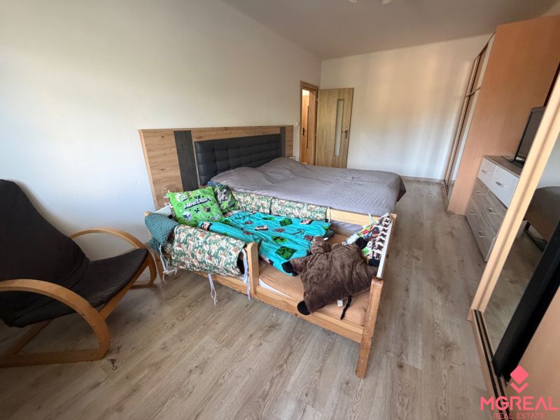 Schlafzimmer in einer 3-Zimmer-Wohnung mit Bett, Sessel und Boden in Holzoptik.
