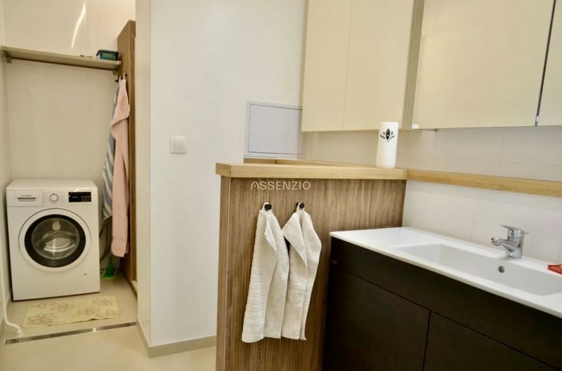 Badezimmer in einer 3-Zimmer-Wohnung mit Waschmaschine, Waschbecken, Holzelementen und Regalen.