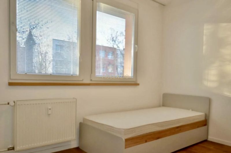 Schlafzimmer in einer 3-Zimmer-Wohnung mit großen Fenstern und einem Boden in Holzoptik.