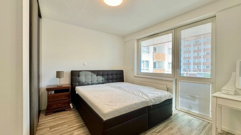 Schlafzimmer in einer 3-Zimmer-Wohnung mit Bett, Nachttisch und Boden in Holzoptik.