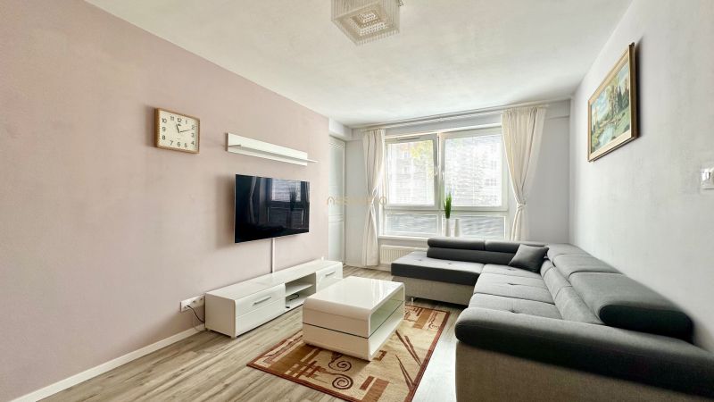 Wohnzimmer mit Ecksofa, Fernseher, Couchtisch und Boden mit Holzdekor.