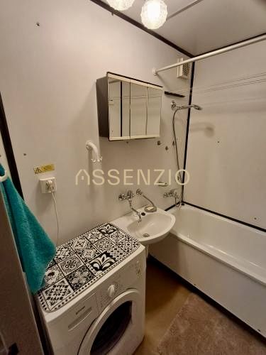 Badezimmer in einem Studio-Apartment mit Badewanne, Waschbecken, Schrank und Waschmaschine.