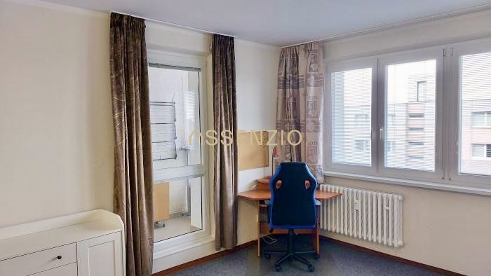 Einzimmerwohnung mit Fenstern, Vorhängen, Heizkörper und einem Tisch mit Stuhl.