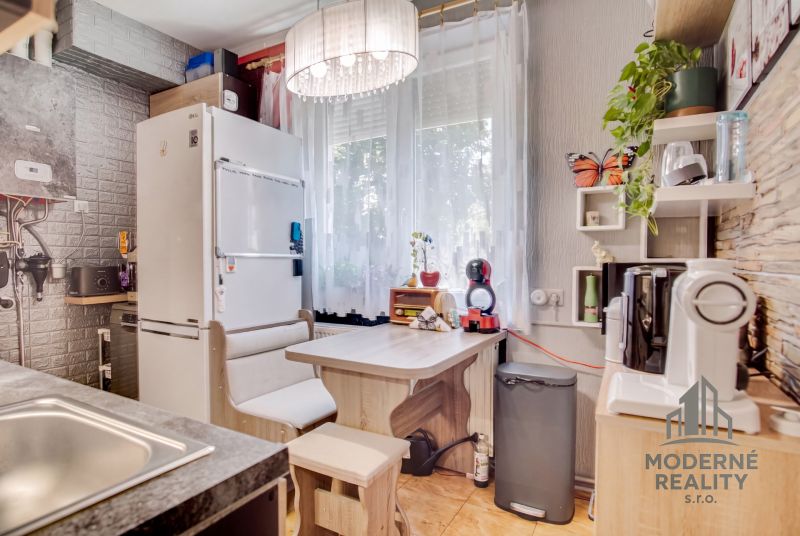 Küche in einer 2-Zimmer-Wohnung mit Essecke und Geräten, Boden mit Holzdekor.