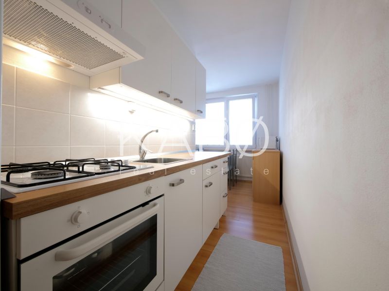 Küche in einer 2-Zimmer-Wohnung mit weißen Schränken und einem Boden in Holzoptik.