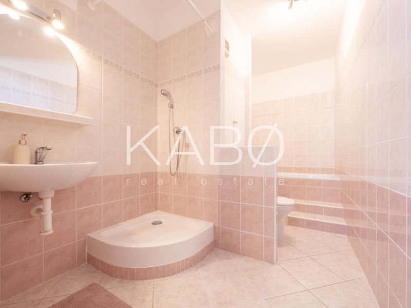 Badezimmer mit Fliesen und Duschkabine in einer Zweizimmerwohnung mit sanften Beigetönen.