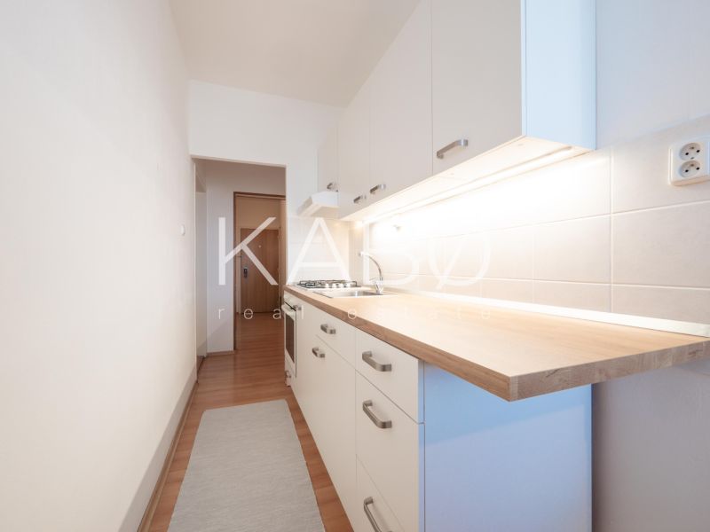 Eine schmale Küche mit weißen Schränken, Fliesenrückwand und Holzboden in einer Zweizimmerwohnung.