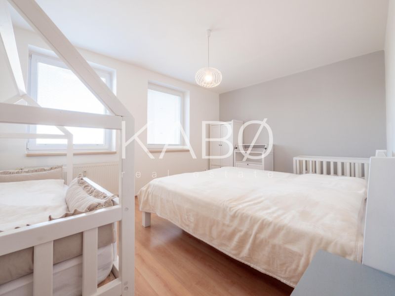 Helles Schlafzimmer in einer 2-Zimmer-Wohnung mit Bett, Kinderbett und Boden in Holzoptik.
