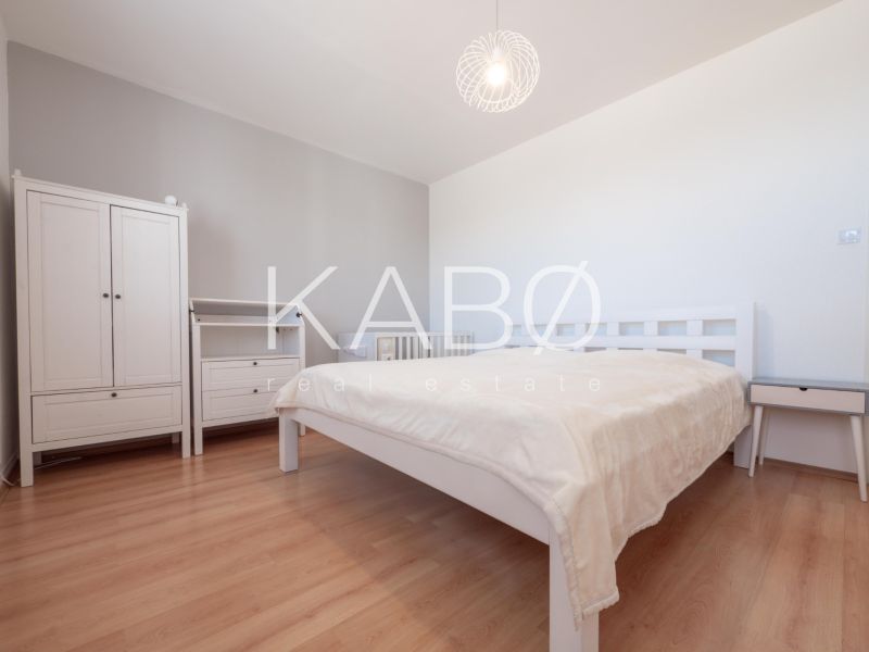 Schlafzimmer in einer 2-Zimmer-Wohnung mit Holzdekorboden, hellen Möbeln und einer Lampe.
