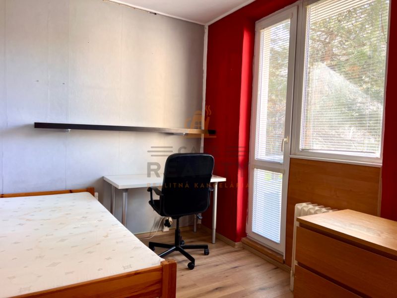 Ein Zimmer in einer 2-Zimmer-Wohnung mit einem Boden in Holzoptik, einem Schreibtisch und einem Bett.