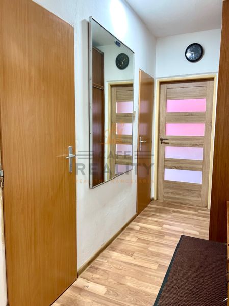 Flur mit Holzboden in einer 2-Zimmer-Wohnung, Spiegel und Uhr an der Wand.