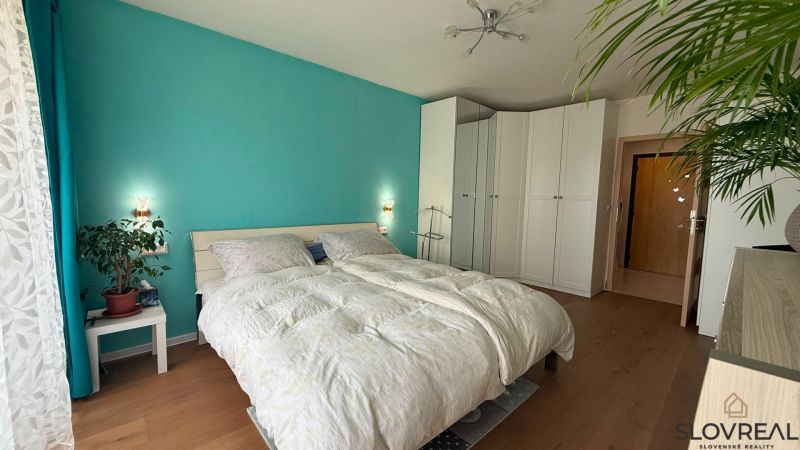 Helles Schlafzimmer mit türkisfarbener Wand, weißen Schränken und Holzboden.