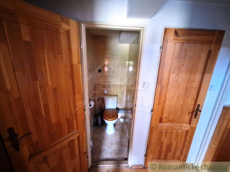 Kleines Badezimmer mit Toilette, zwei Türen, Boden mit Holzdekor.
