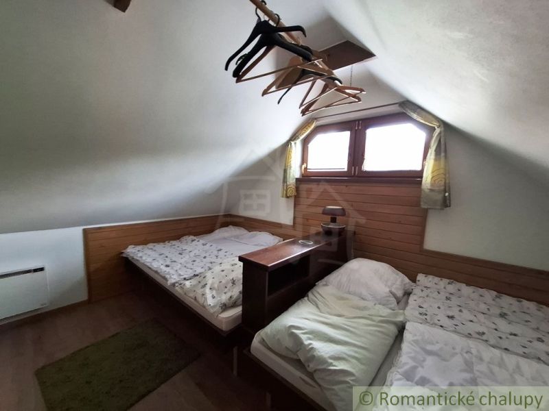 Dachboden mit zwei Betten, Holzboden, Kleiderhaken, kleines Fenster, niedrige Decke.