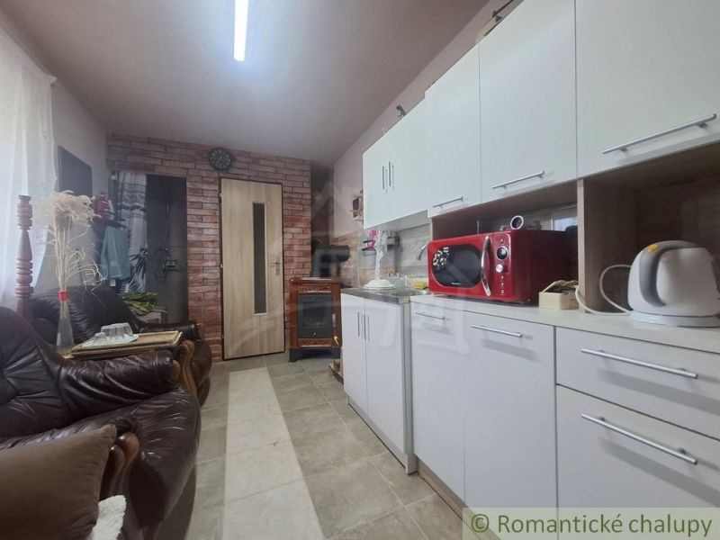 Eine Küche in einer Hütte mit weißen Schränken, einer roten Mikrowelle und Ledersofas.