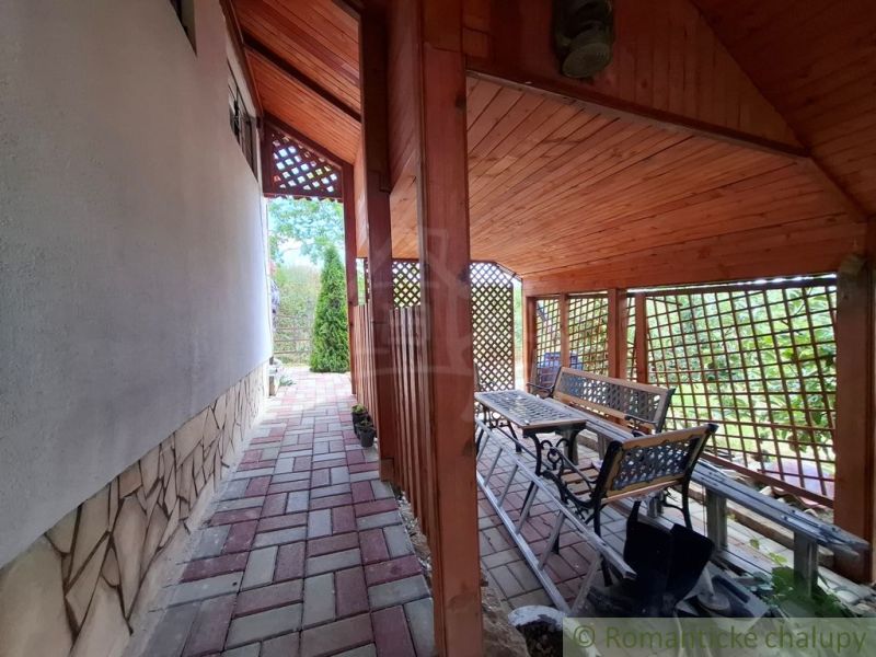 Eine Terrasse bei der Hütte in Gbelce mit Pflastersteinen und Gartenmöbeln unter einem Holzdach.