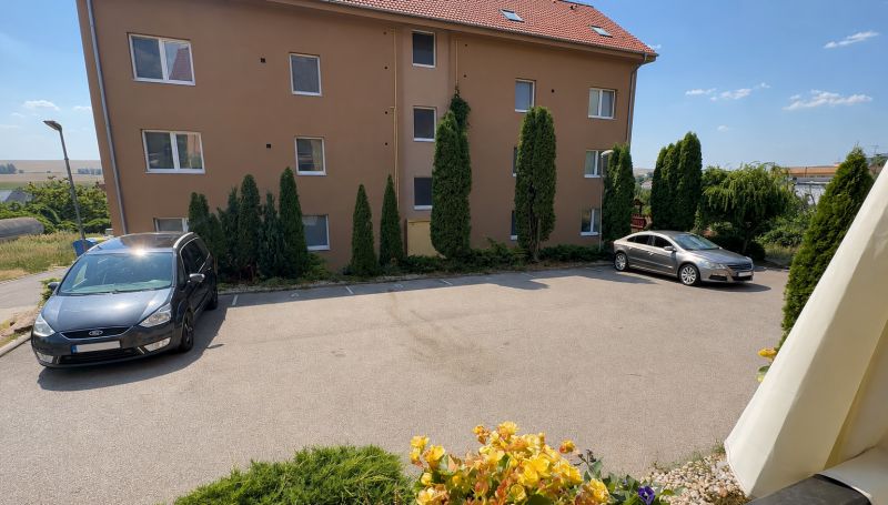 Parkplatz vor einem Wohnhaus in Veľký Lapáš mit Autos und umliegendem Grün.