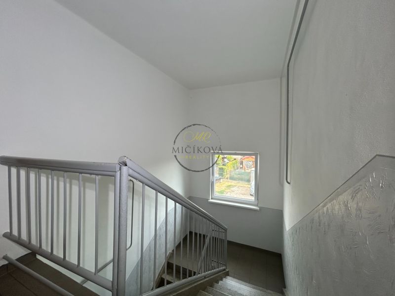 Eine Treppe mit Fenster in einer 2-Zimmer-Wohnung, die Wände sind weiß mit einem Metallgeländer.