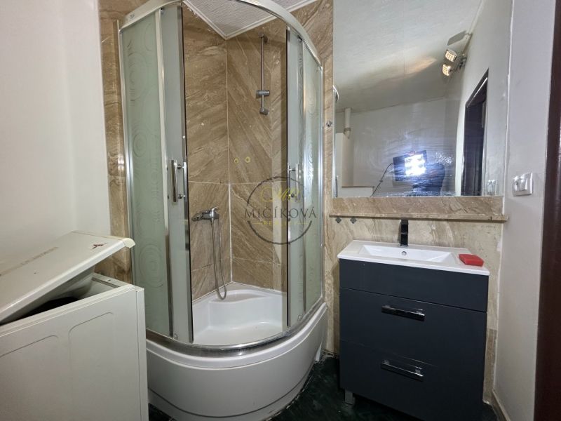 Badezimmer mit Dusche, dunklem Schrank und Spiegel in einer Zweizimmerwohnung.