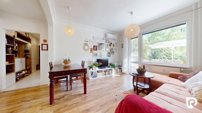 Wohnzimmer in einer 3-Zimmer-Wohnung mit Holzboden, großem Fenster und dekorativen Elementen.