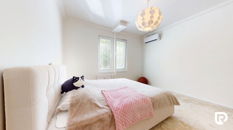 Helles Schlafzimmer mit großem Bett, zwei Fenstern und Klimaanlage in einer 3-Zimmer-Wohnung.
