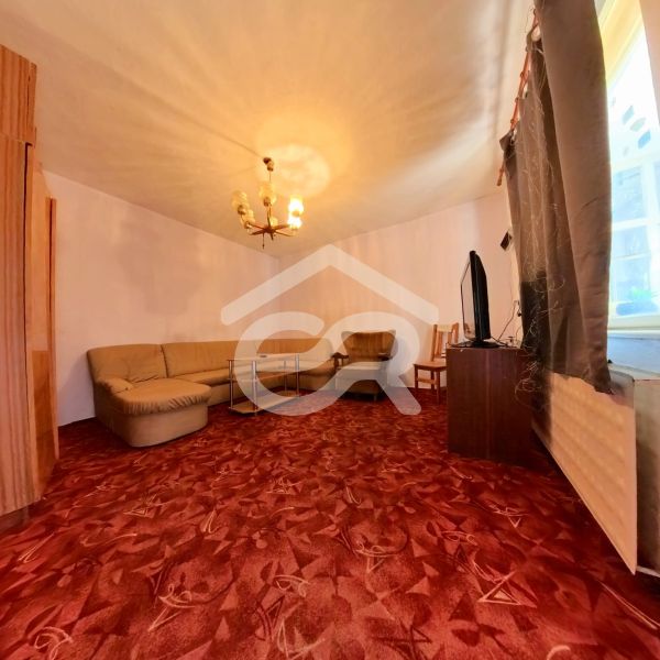 Wohnzimmer in einem Einfamilienhaus mit Ecksofa und bordeauxfarbenem Teppich.