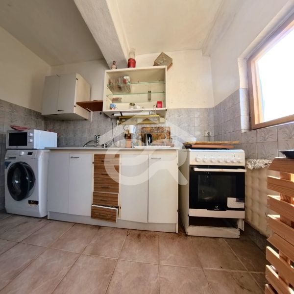 Küche in einem Einfamilienhaus mit Keramikboden, Schränken, Herd, Mikrowelle und Waschmaschine.