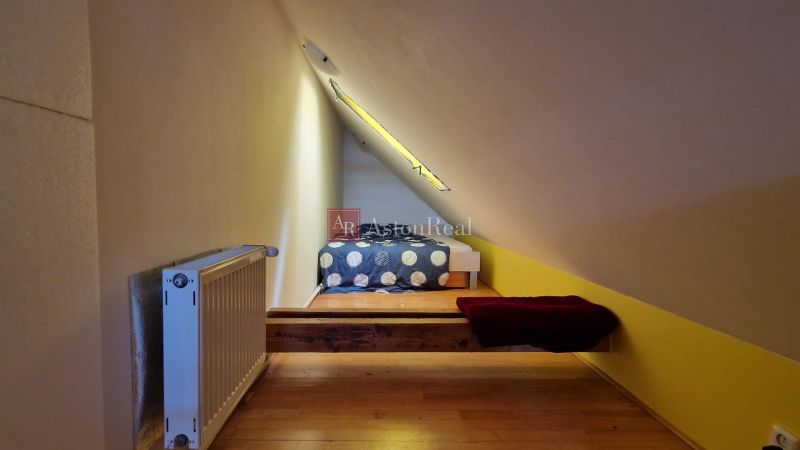 Dachzimmer mit schräger Decke, Heizkörper und Boden mit Holzdekor.