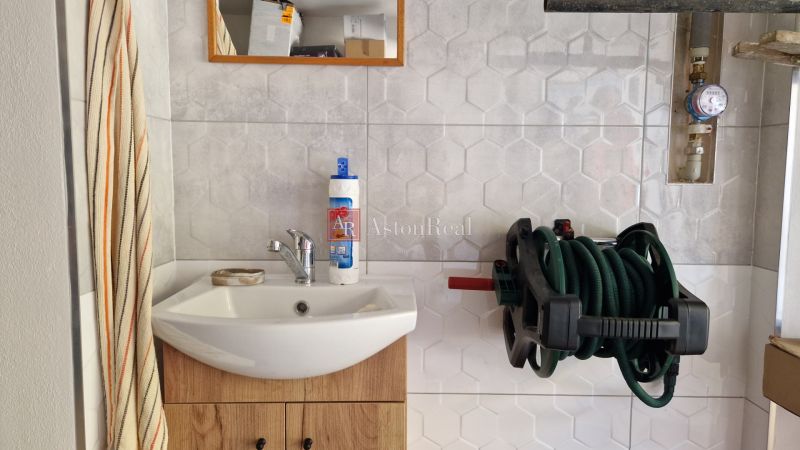 Badezimmer in einer 2-Zimmer-Wohnung mit Waschbecken, Spiegel und Wandhalterung für einen Schlauch.