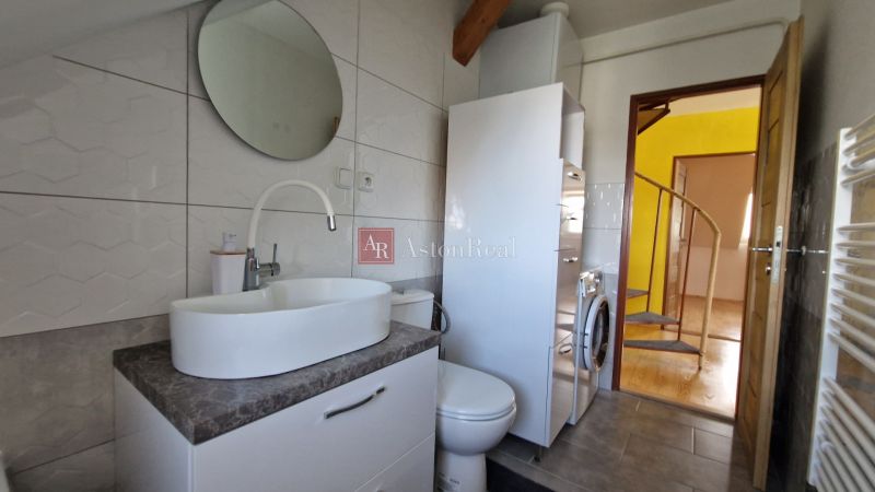 Badezimmer in einer 2-Zimmer-Wohnung mit Waschbecken, rundem Spiegel und Waschmaschine.