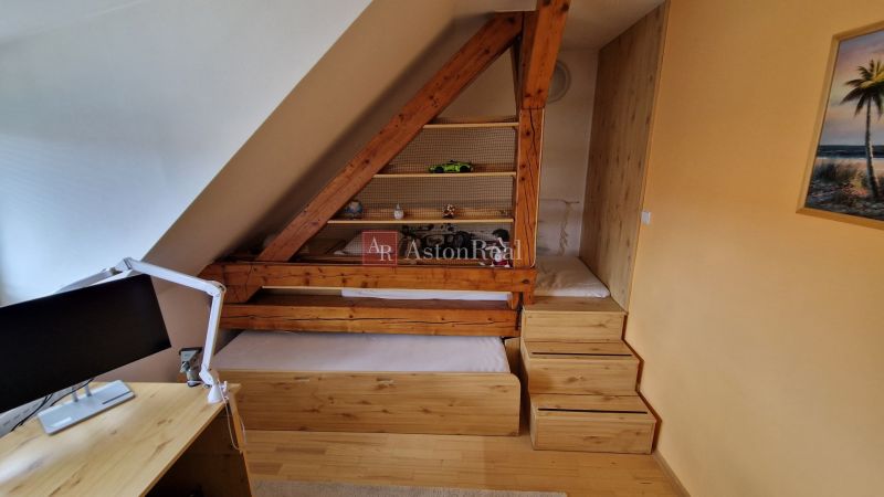 Podkrovná miestnosť s drevenými prvkami, posteľou a pracovným stolom v 2-izbovom byte.

Dachgeschosszimmer mit Holzelementen, Bett und Schreibtisch in einer 2-Zimmer-Wohnung.