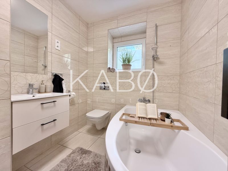 Badezimmer mit Badewanne und Waschbecken in einer 2-Zimmer-Wohnung, beige Fliesen.