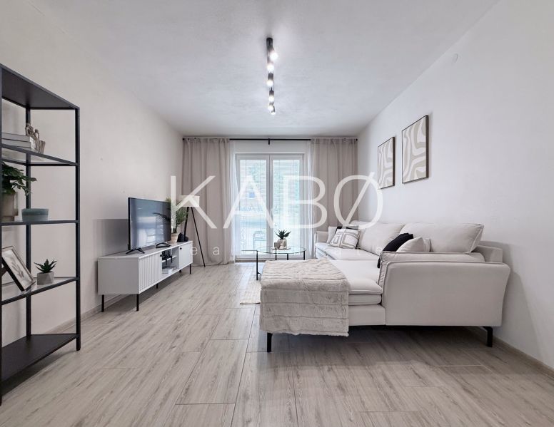Wohnzimmer in einer 2-Zimmer-Wohnung mit Sofa, Fernseher und Holzboden.