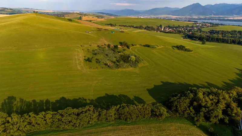 Weitläufige grüne Felder und Hügel in Liptovský Trnovec, die einen Blick auf ungewöhnliche Immobilien bieten.