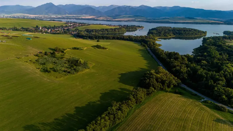 Liptovský Trnovec bietet weitläufige Grünflächen mit einem See, umgeben von Waldgebieten und Feldern.
