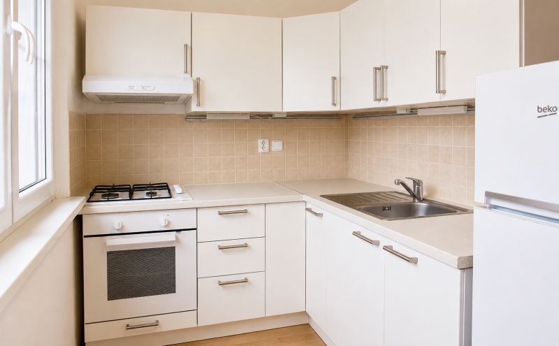 Küche mit weißen Schränken und Geräten in einer Zweizimmerwohnung, Boden mit Holzdekor.