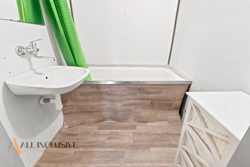 Badezimmer in einer 3-Zimmer-Wohnung mit Badewanne, Waschbecken und Boden in Holzoptik.