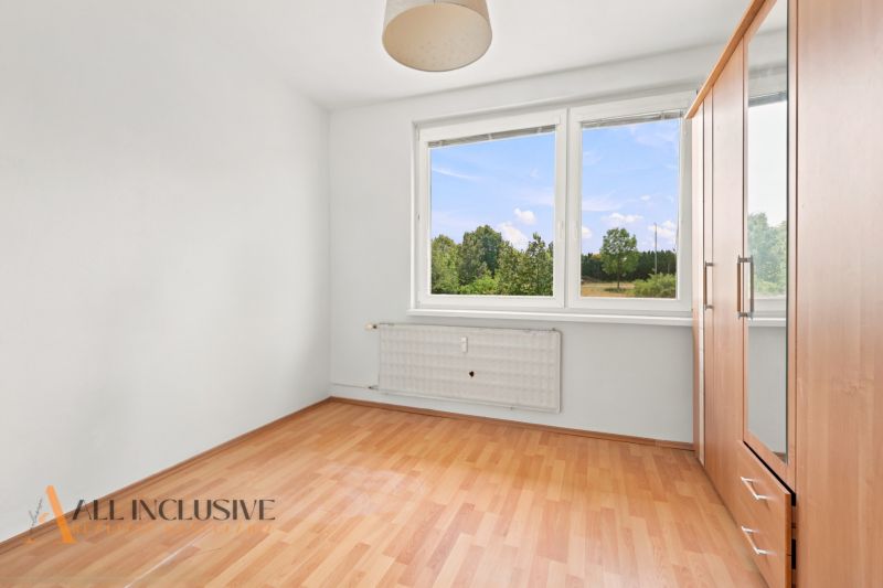 Ein leerer Raum mit einem großen Fenster und einem Boden in Holzoptik in einer 3-Zimmer-Wohnung.