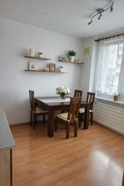 Essbereich mit Tisch, Stühlen und Regalen auf einem Boden mit Holzdekor in einer 3-Zimmer-Wohnung.
