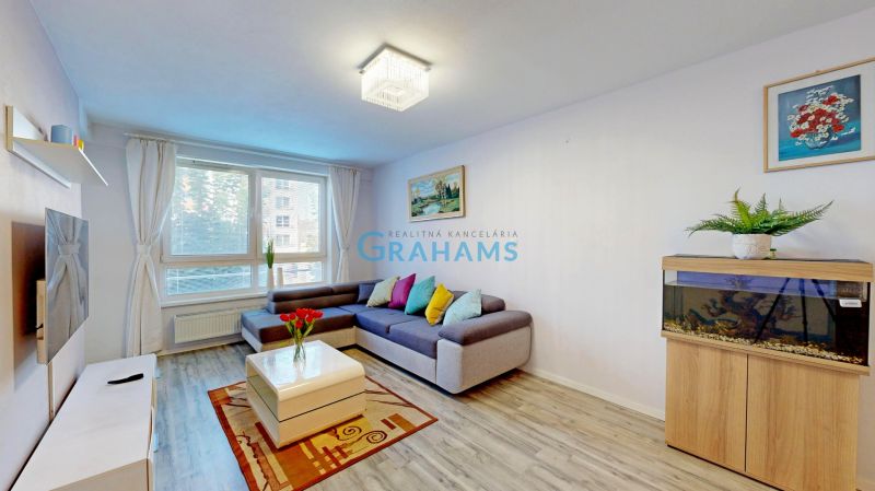 Wohnzimmer in einer 3-Zimmer-Wohnung mit Sofa, Aquarium, Pflanze und Holzboden.