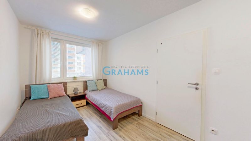 Zwei Betten mit bunten Kissen und ein Boden mit Holzdekor in einer 3-Zimmer-Wohnung.
