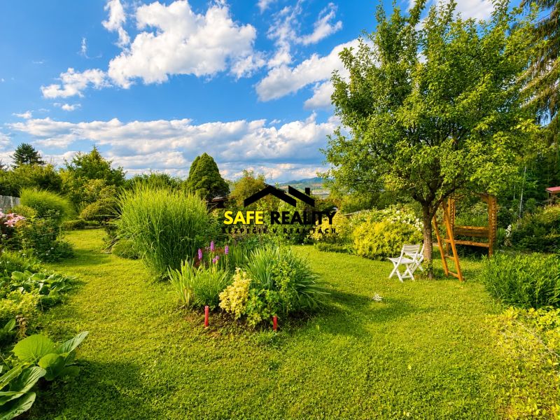 Ein Garten bei einer Hütte in Žilina mit Bäumen, Blumen und weißen Gartenmöbeln.