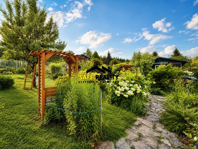 Ein Garten bei einer Hütte in Žilina mit einer Holzpergola und Blumenbeeten.