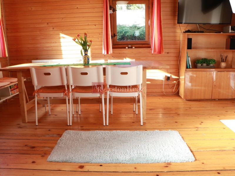 Innenraum einer Hütte mit einem Esstisch, weißen Stühlen und einem Boden mit Holzdekor.